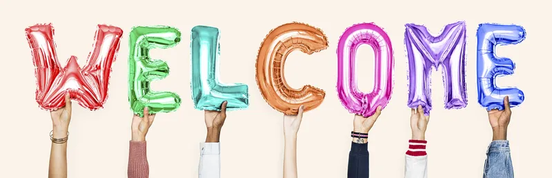 Diverse hands hold up multi-colored balloon letters that say WELCOME